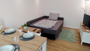 A compact room with a bed, a small table set for dining, a TV, and a plant. - FeWo Wildflecken - Holiday apartment Rhön new building 2021 (Wildflecken)