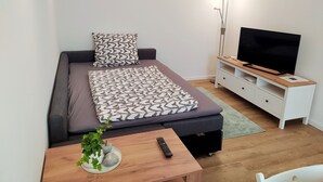 A modern bedroom with a bed, a TV, a bedside table, and a floor lamp. - FeWo Wildflecken - Holiday apartment Rhön new building 2021 (Wildflecken)