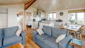 A spacious living area with a kitchen, a dining table, and a cozy seating arrangement. - Luxurious and contemporary lodge with stunning countryside views. (Bretby, Derbyshire)