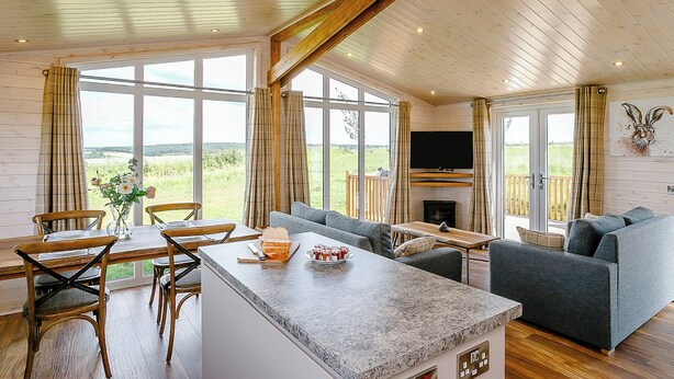 A spacious living area with a large window, a fireplace, and a television. - Luxurious and contemporary lodge with stunning countryside views. (Bretby, Derbyshire)