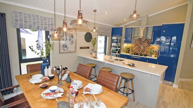 Une cuisine moderne dotée d’un îlot central, de luminaires suspendus et d’un coin repas avec une table et des chaises en bois.