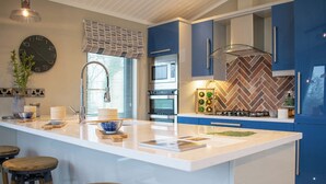 Une cuisine moderne dotée d’un îlot central, de tabourets de bar, d’une horloge et d’un pare-feu en motif chevrons.