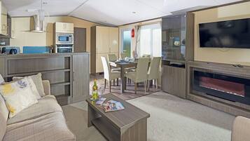 A modern living room with a sofa, coffee table, TV, kitchen area, and dining space.