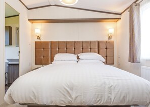 Une chambre à coucher avec une tête de lit capitonnée, deux lampes de chevet et un grand lit recouvert de linge de lit blanc.