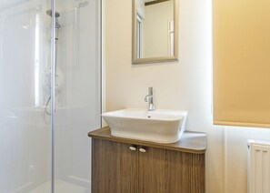 Une salle de bain avec une douche à parois de verre, un meuble-lavabo en bois avec un lavabo blanc et un miroir au-dessus du lavabo.