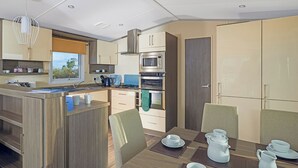 Et moderne køkken med en central ø, indbygget ovn, mikroovn og et spiseområde med et bord til fire.