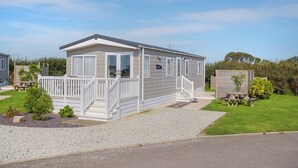 En etagers mobilhome med en veranda, en lille terrasse og en grusvej.