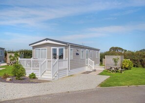 Une maison mobile de plain-pied, dotée d’un porche à l’avant, d’une petite terrasse et d’une allée en gravier.