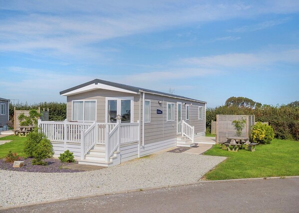 Une maison mobile de plain-pied, dotée d’un porche à l’avant, d’une petite terrasse et d’une allée en gravier.