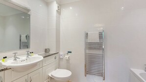 A modern bathroom with a white sink, two faucets, a toilet, a mirror, and a towel rack.