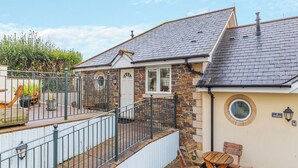 A house with a stone exterior, a tiled roof, and a fenced yard with a play area.