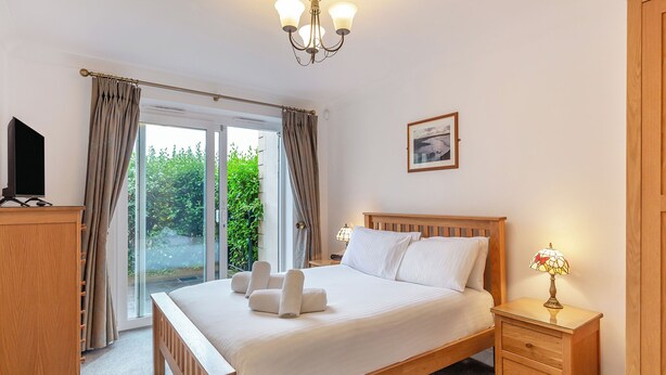 A bedroom with a bed, bedside tables, a TV, a chandelier, and a view through the window.