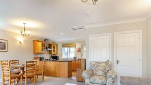 A modern kitchen with wooden cabinets, a dining area with a wooden table and chairs, a patterned armchair, and a sofa.
