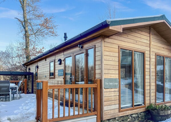 Un chalet en bois doté d’une terrasse, de grandes fenêtres et d’une enseigne indiquant « The Oaks Lodge ».
