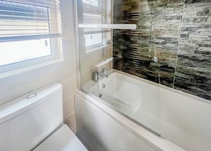 Et badeværelse med badekar, toilet og et vindue med skodder.