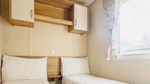 Una camera compatta con due letti, mobili in legno, una finestra con tenda a fiori e un interruttore a parete.
