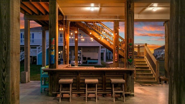 A wooden bar area with a staircase leading to upper levels, benches, and string lights. - Welcome to Sunset Dazed! See special rates & come enjoy the beach! (Galveston)