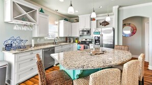A modern kitchen with white cabinets, a granite island, and wicker chairs. - Welcome to Sunset Dazed! See special rates & come enjoy the beach! (Galveston)