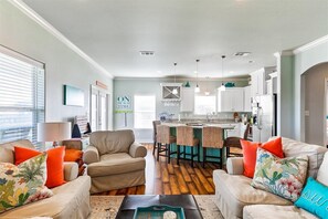 Un salon moderne avec un canapé beige, une table basse et un coin cuisine à l’arrière-plan.