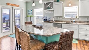 A kitchen with a large island, white cabinets, and a view of the outdoors. - Welcome to Sunset Dazed! See special rates & come enjoy the beach! (Galveston)