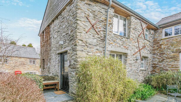 Un bâtiment en pierre avec un toit en pente, une porte et une fenêtre.