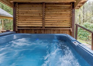 A hot tub with a wooden deck and a wooden ceiling, surrounded by greenery. - Timber lodge set in an elevated position with views of the lake. (Webbery, Bideford)