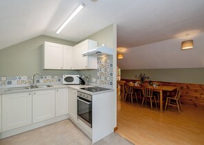 Une cuisine moderne avec des meubles blancs, un four à micro-ondes et un four traditionnel. On y trouve également un coin repas avec des chaises et une table en bois.