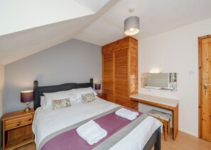 Une chambre à coucher comprenant un lit, une table de chevet, une armoire en bois, un bureau et un miroir.