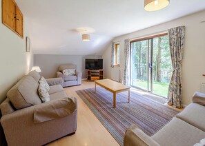 Un salon avec un canapé, une table basse, un téléviseur et une grande fenêtre avec des rideaux.