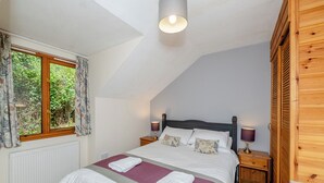 Una camera da letto con soffitto spiovente, un letto con biancheria bianca, due lampade da comodino, una finestra con tende e un termosifone.
