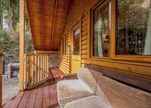 Une cabane en rondins avec une véranda en bois, un banc et de grandes fenêtres.