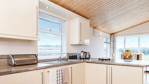 A modern kitchen with a wooden ceiling, white cabinets, a stainless steel toaster, and a window with a view.
