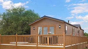 Une cabane en bois dotée d’une terrasse, de grandes fenêtres et d’une cheminée.