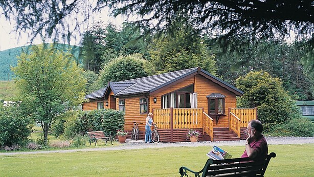 A wooden cabin with a porch, a bench, and a bicycle. - Log cabin with one double with en suite shower and two twin. (Ettrick Valley, Nr Hawick)