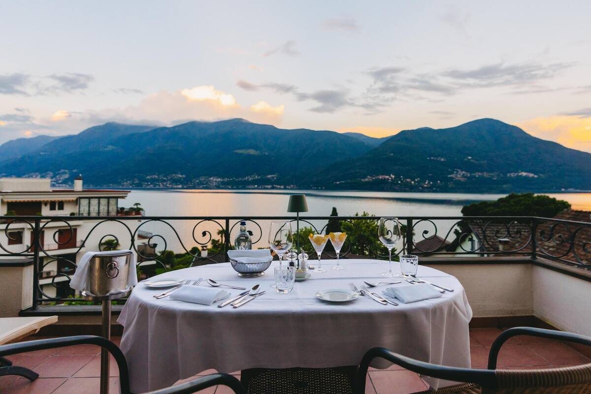 Mesa redonda dispuesta para comer con vistas a montañas y un lago.