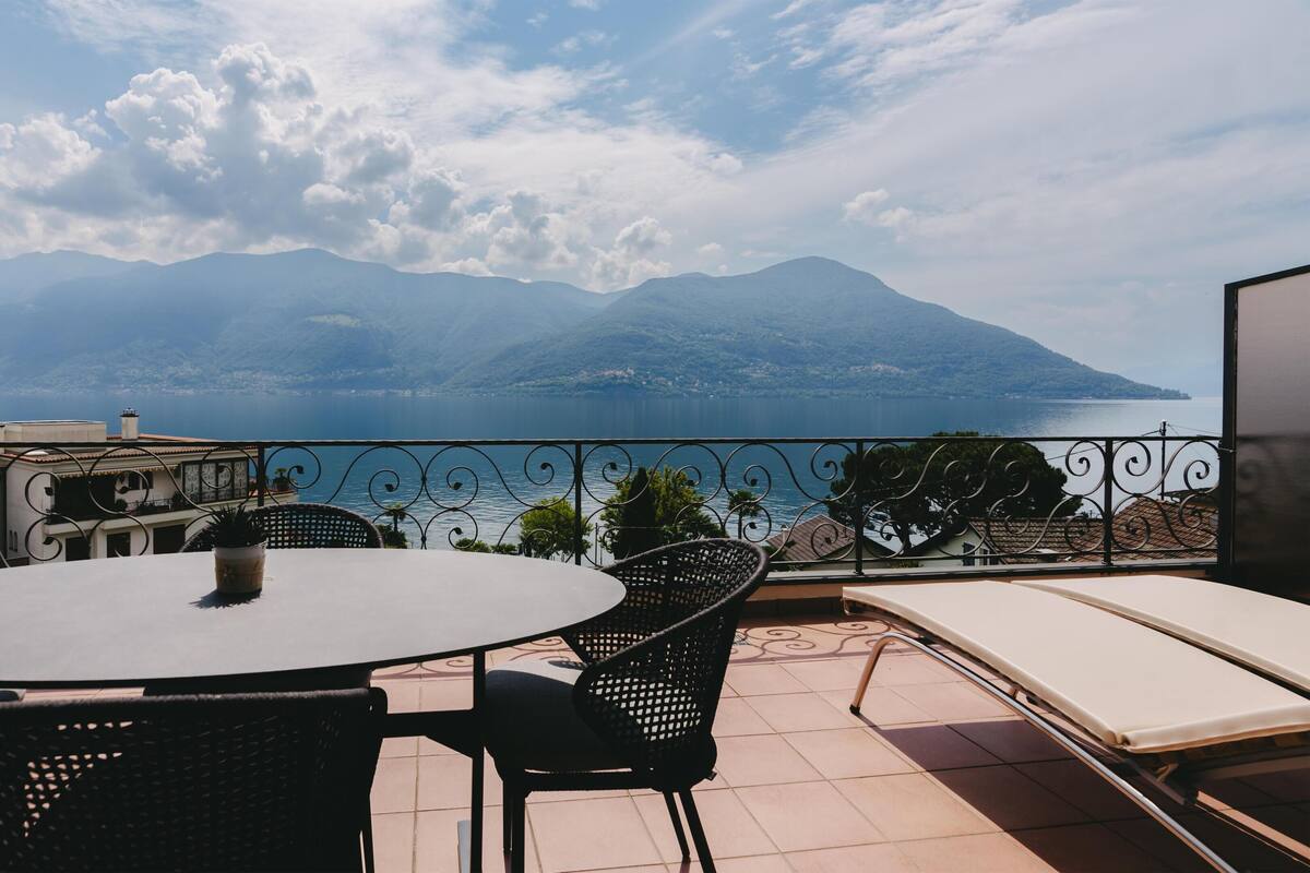 Un balcón con una mesa redonda y sillas, con vista a un lago y montañas.