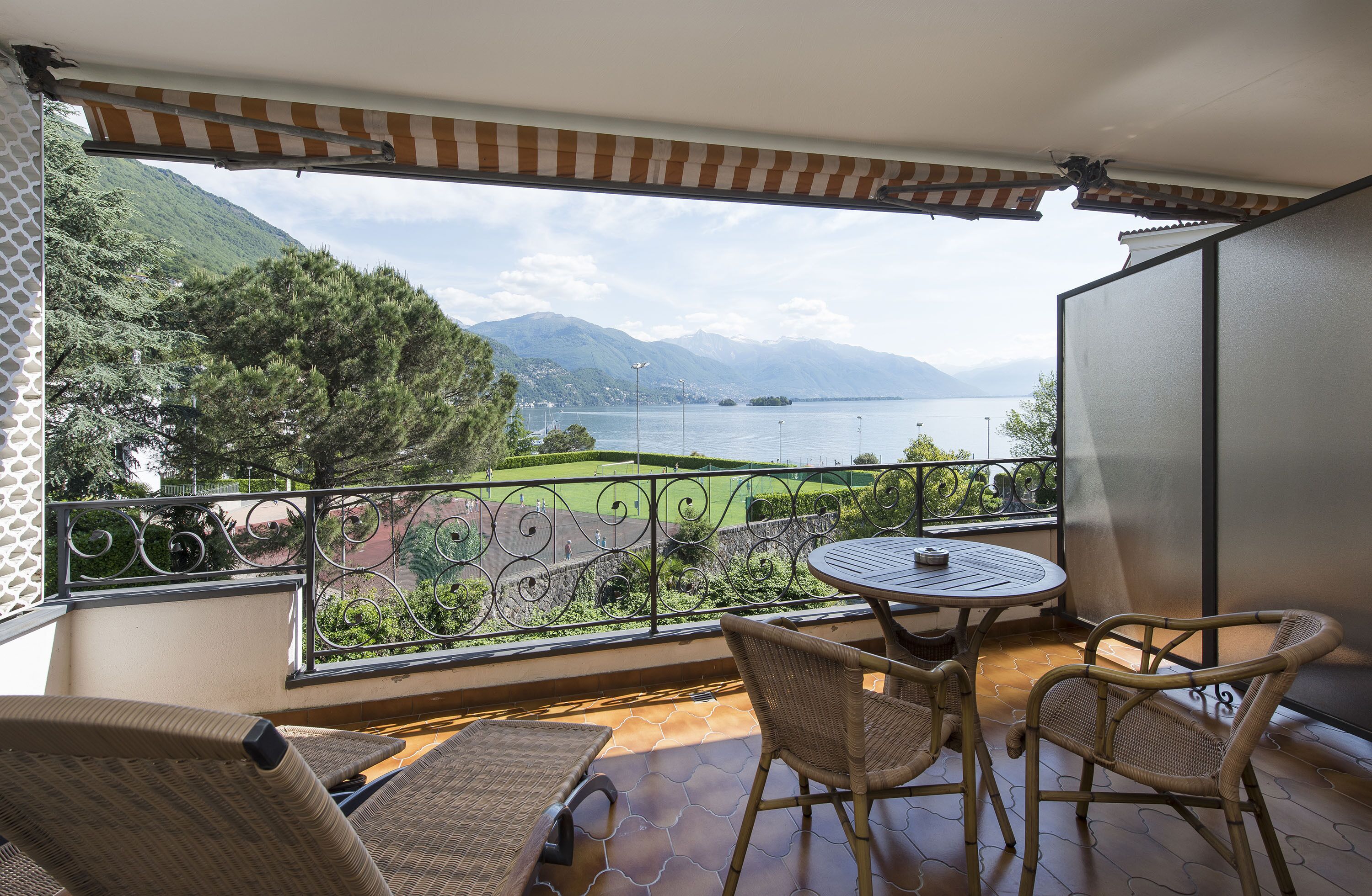 Un balcón con mobiliario de mimbre, vista a un lago y montañas, y barandilla estampada.