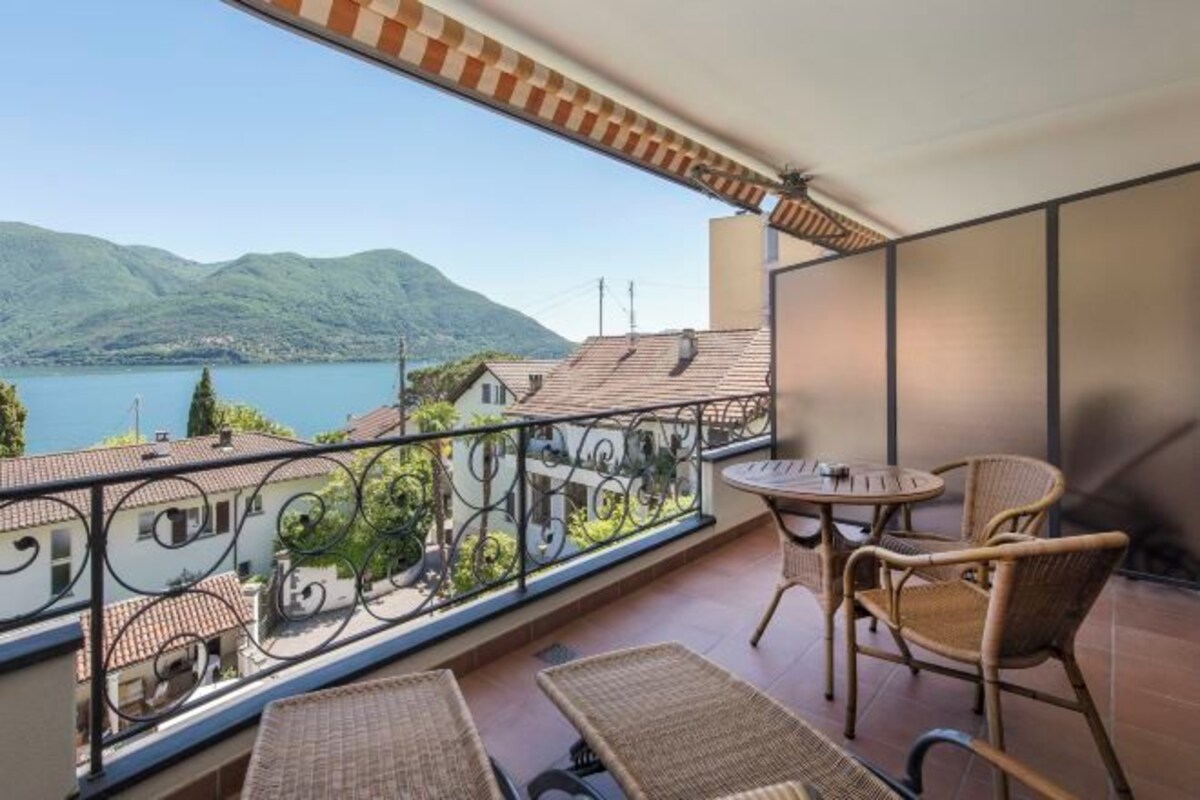 Un balcón con mobiliario de mimbre y vistas a un lago y montañas.