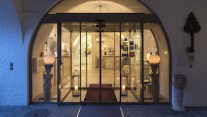Entrada de hotel con puerta de vidrio, felpudo y un pilar de piedra.
