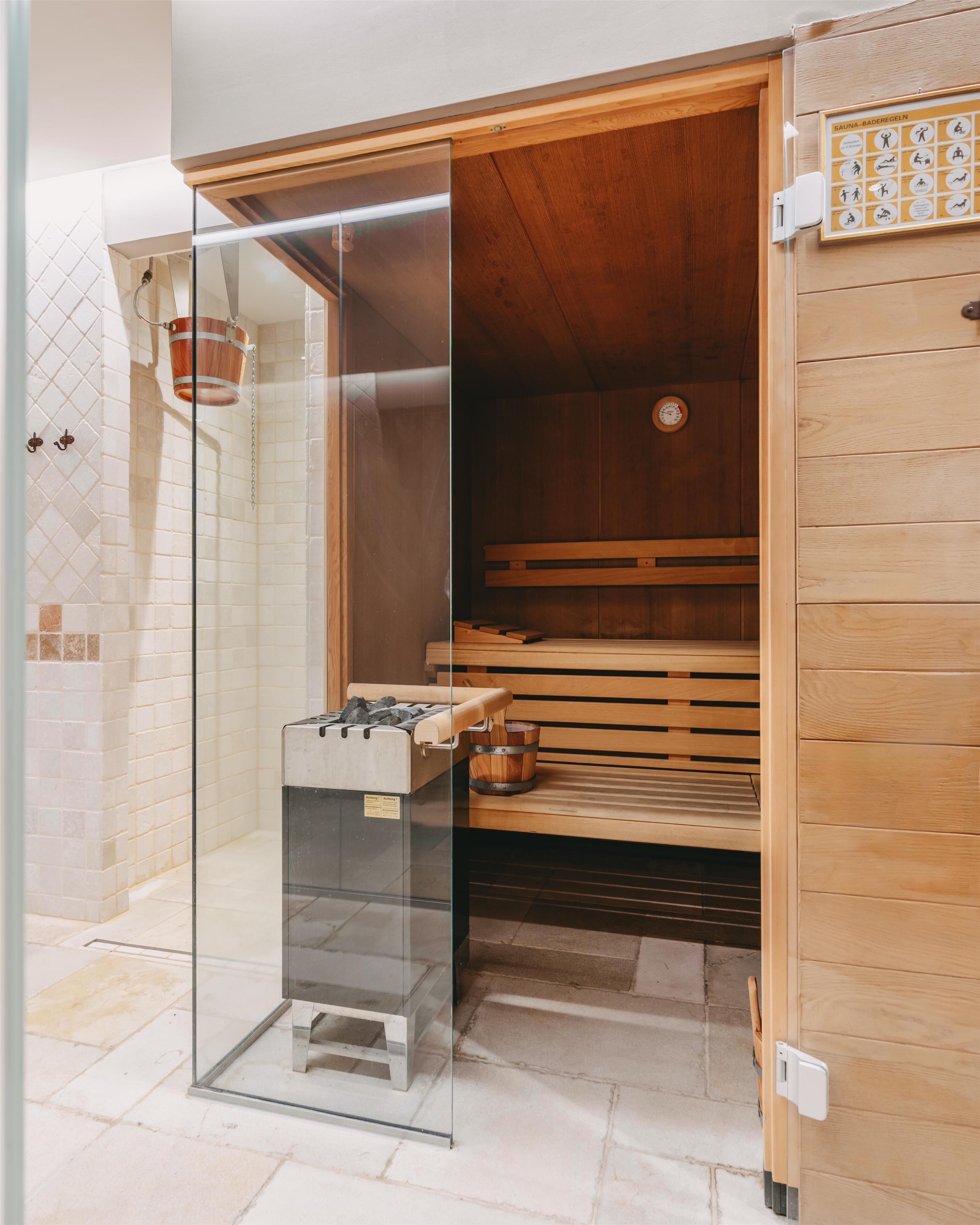 Een sauna met glazen wand, houten banken en een houten wand, plus een sauna-bordje.