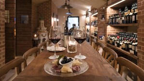 Una mesa de madera con copas de vino, una vela y una tabla de quesos en una habitación con paredes de ladrillo y una vinoteca al fondo.
