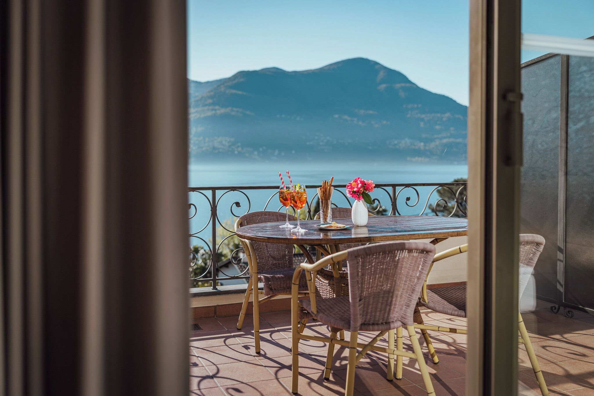 A balcony with a table and chairs, a view of a mountain, and a body of water.