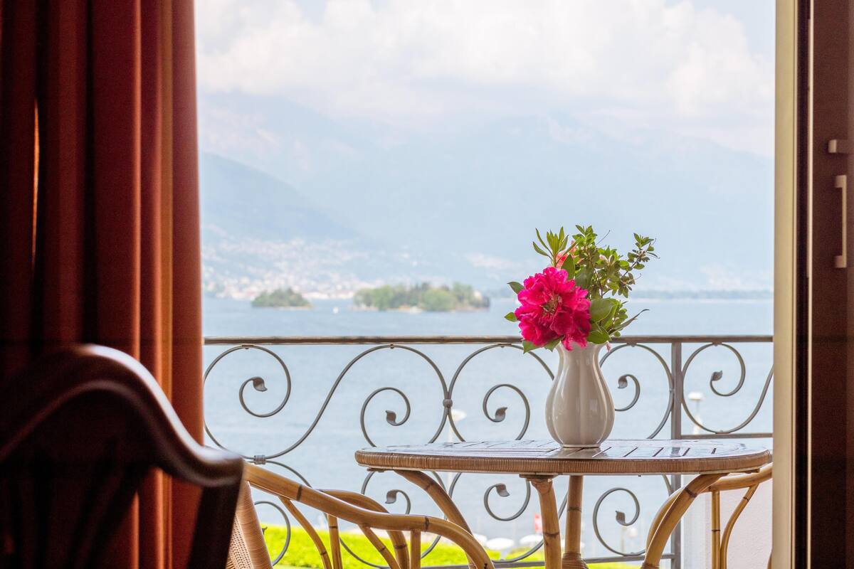 Un balcón con una mesa y una silla, un jarrón con flores y vistas a un lago y montañas.
