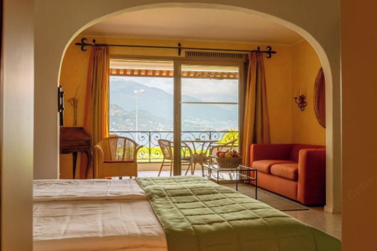 Una habitación con una cama, un sofá rojo, una mesa de comedor con sillas y vistas a las montañas a través de un ventanal grande.