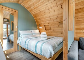 A cozy bedroom with a wooden ceiling, a bed with striped bedding, a bench, and a small wall-mounted light fixture.