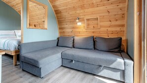 A cozy room with a wooden ceiling, a grey sofa, a bed with a striped duvet, and a wall-mounted light fixture. - 0 bedroom accommodation in Great Busby (Great Busby)