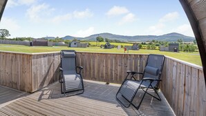 A wooden deck with two reclining chairs and a view of a rural landscape with buildings and hills. - 0 bedroom accommodation in Great Busby (Great Busby)