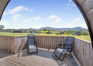 Une terrasse en bois avec deux chaises longues et une vue sur un paysage rural, avec des bâtiments et des collines.