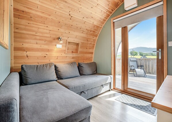 Una stanza accogliente con soffitto in legno, un divano grigio e una porta scorrevole in vetro che dà su una terrazza esterna.