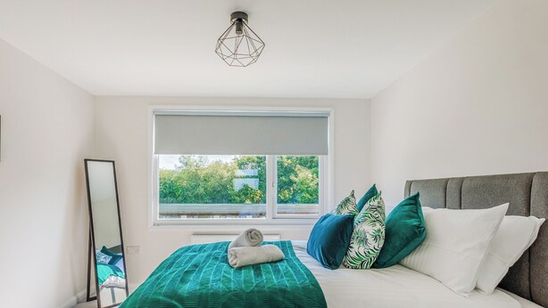 Un dormitorio con cama, ventana, espejo y lámpara en el techo.